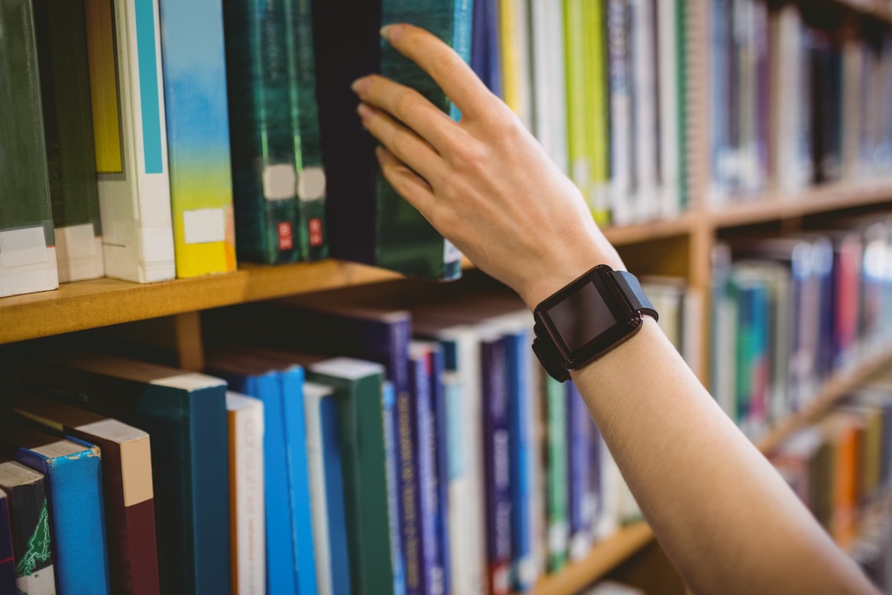 Student picking book in library wearing smart watch at the university.jpeg