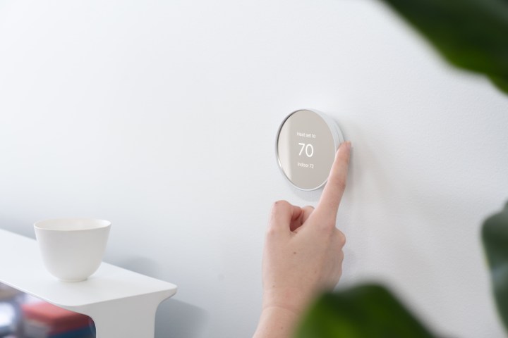 Finger touching the side of Google Nest Thermostat (2020).