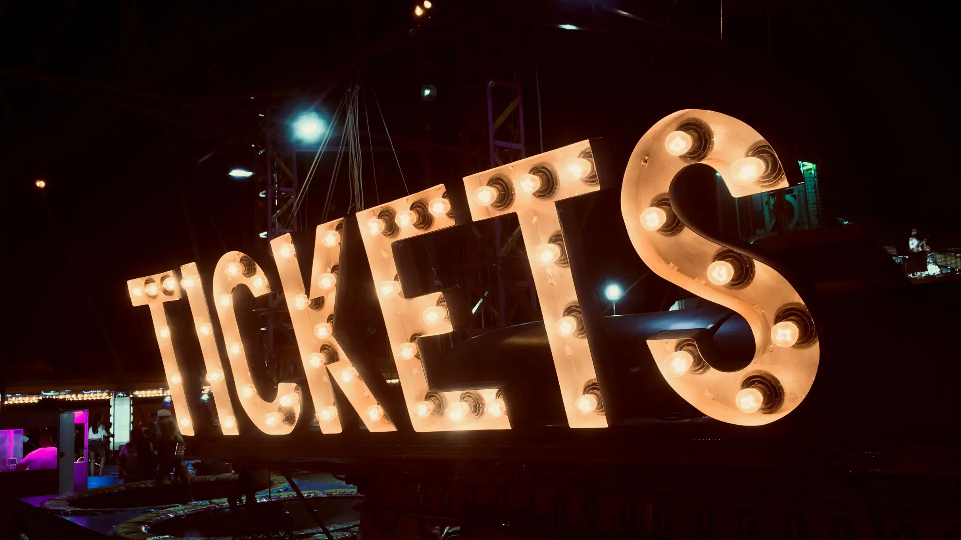 Large illuminated sign spelling TICKETS with marquee-style lights at an event venue at night