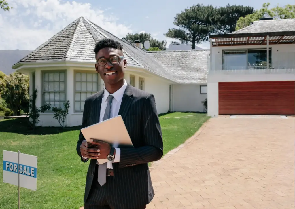 Real estate agent in suit holding clipboard in front of house with 'For Sale' sign and scenic backdrop