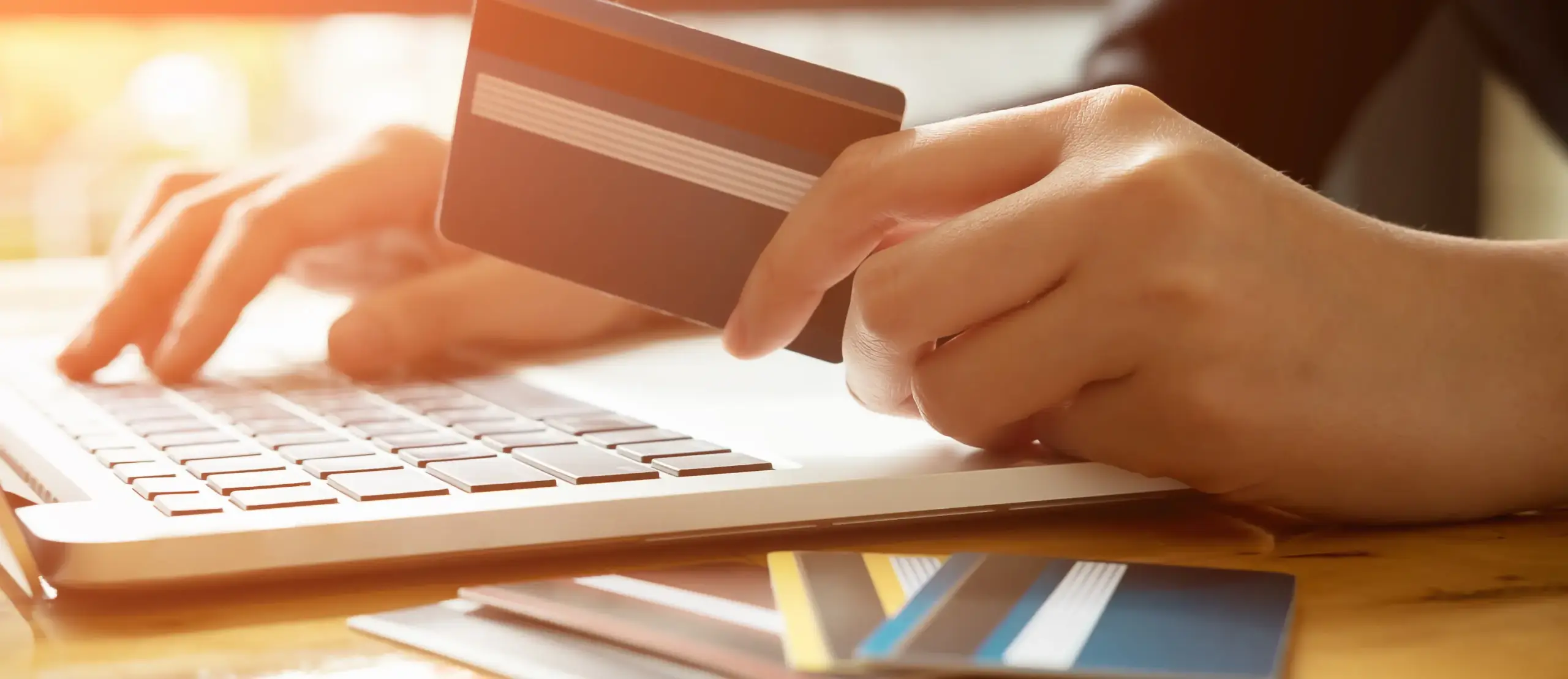 Person using laptop for online shopping with credit card in hand and multiple cards on table