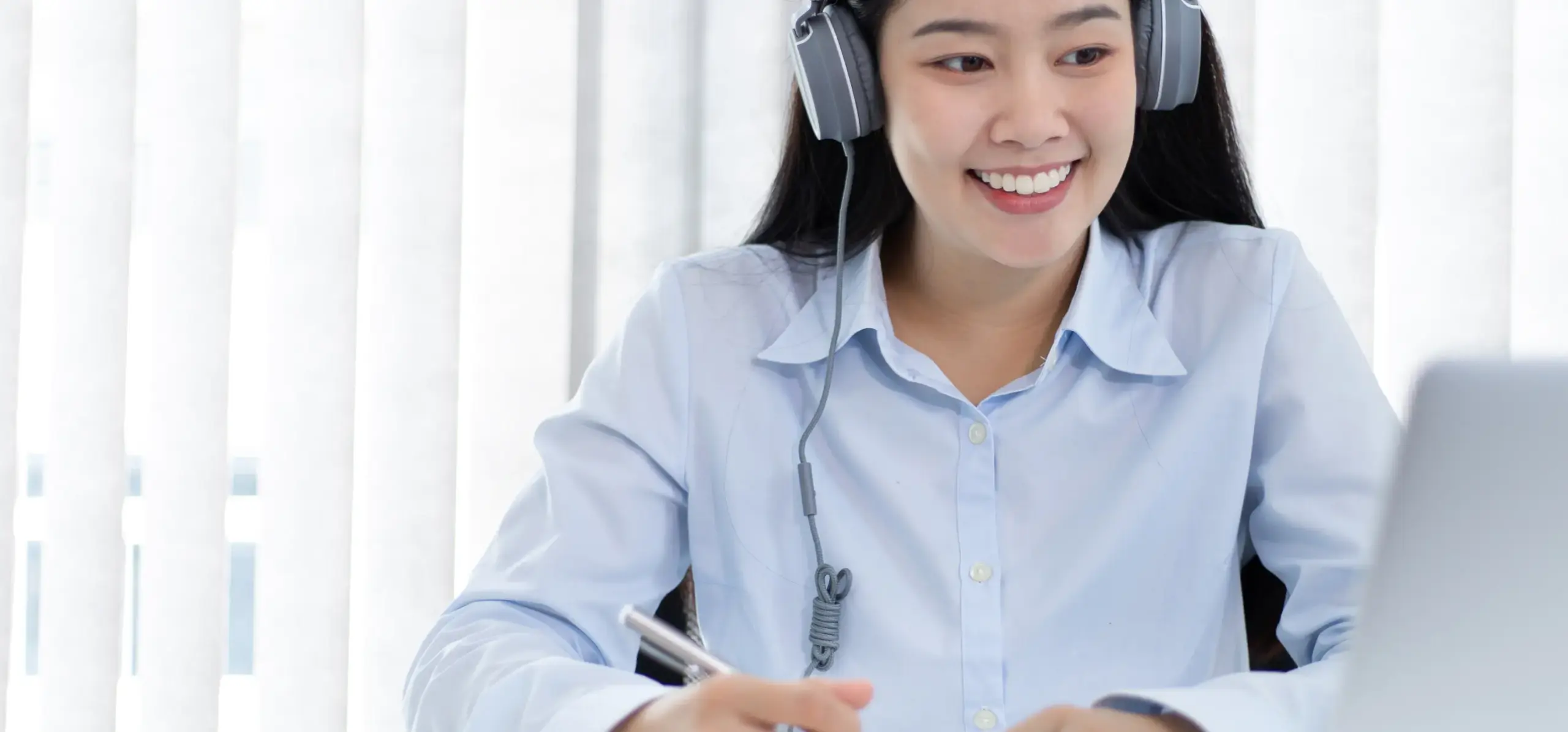 Smiling remote worker in headphones at laptop during virtual meeting or online class in bright indoor setting